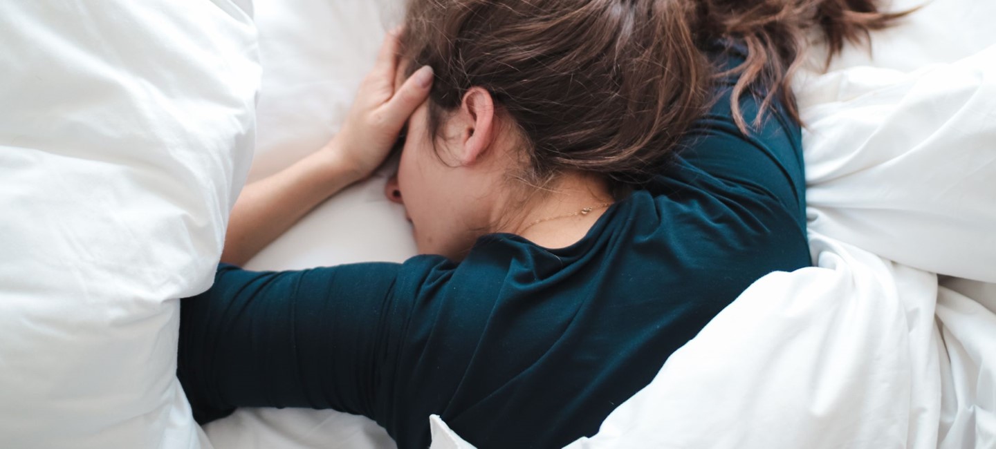 WCN-21_non-headache-symptoms-in-migraine-2320x1000px.jpg Woman lying in bed on her stomach while holding head.